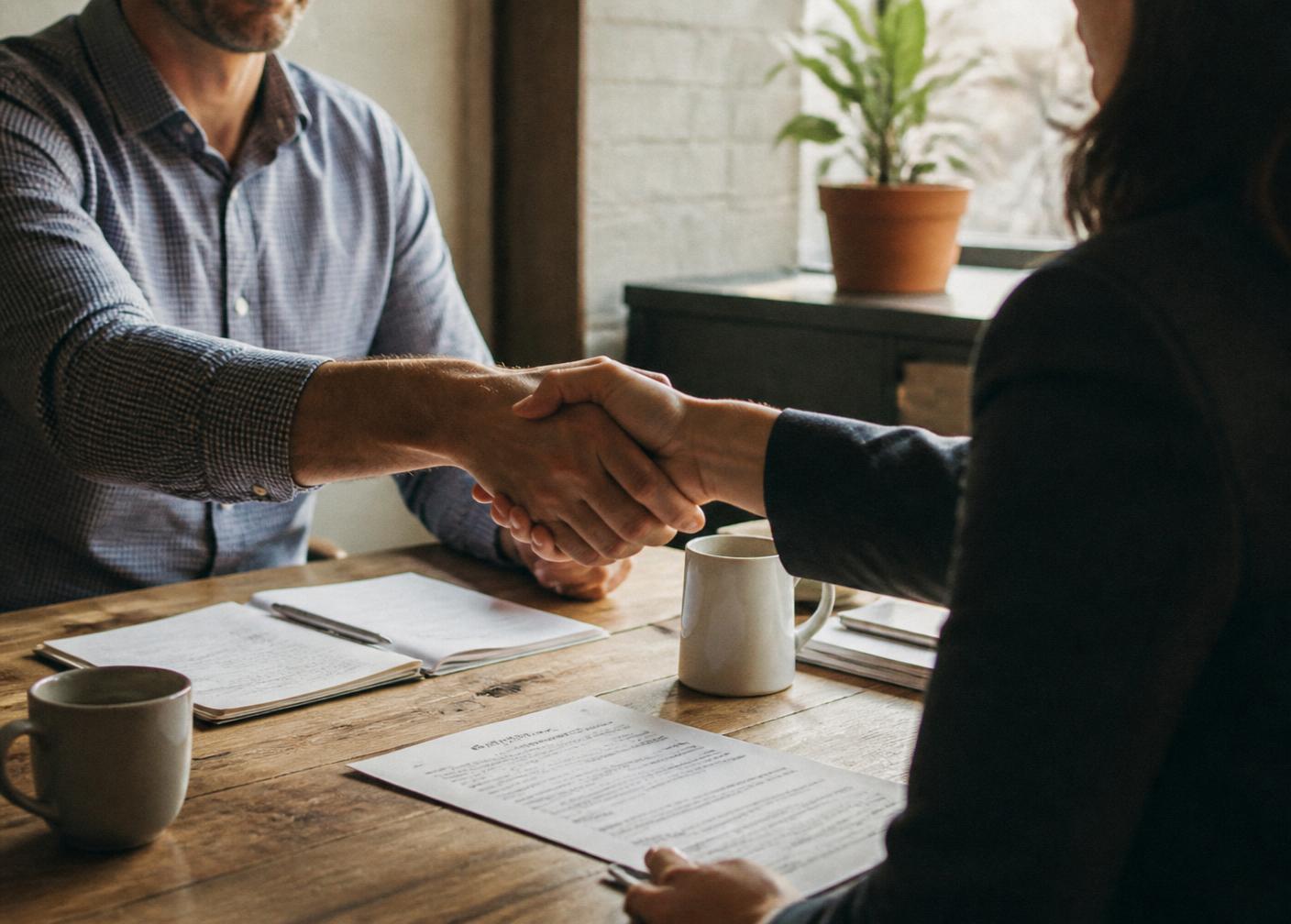 Two people shaking hands over paperwork